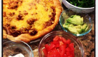 Taco pie covered in melted cheese and veggies on the side.
