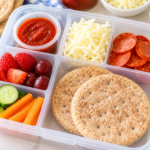 Homemade pizza lunchables with sandwich thins, pepperoni, mozzarella, pizza sauce, fruit, and vegetables