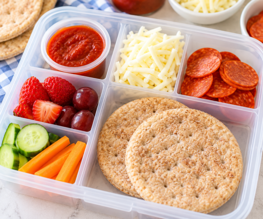 Homemade pizza lunchables with sandwich thins, pepperoni, mozzarella, pizza sauce, fruit, and vegetables