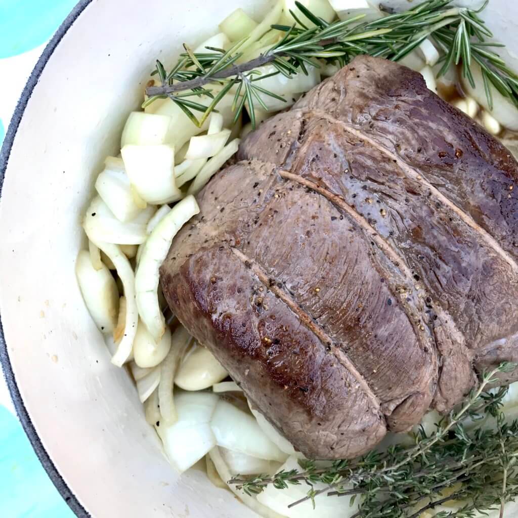 40-cloves-garlic-beef-roast-2 - Mom to Mom Nutrition Close up of 40 cloves of garlic beef roast on a white plate with garlic surrounding it.