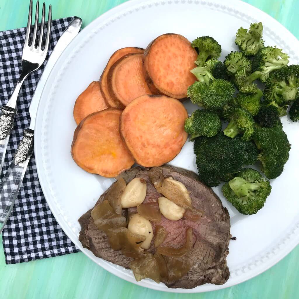 40-cloves-garlic-beef-roast-5 - Mom to Mom Nutrition 40 cloves of garlic beef roast sliced on a white plate with sweet potatoes and broccoli.