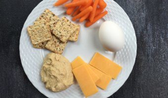 Toddler snack ideas, crackers, carrots, eggs, cheese, and hummus on a plate.